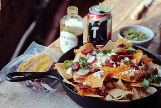 A cast iron frying pan filled with corn chips topped with cheese, chorizo and jalapenos.