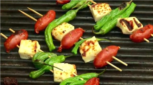 Skewers of Chorizo, cheese and padron peppers cooking on a grill.